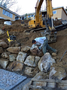 Men and excavator working on boulder retaining wall